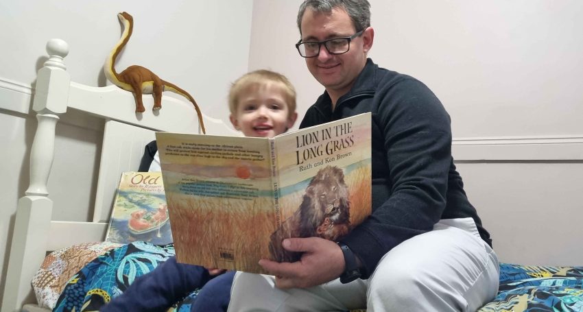 The Rev'd Andrew Schmidt and son John reading Lion in The Long Grass