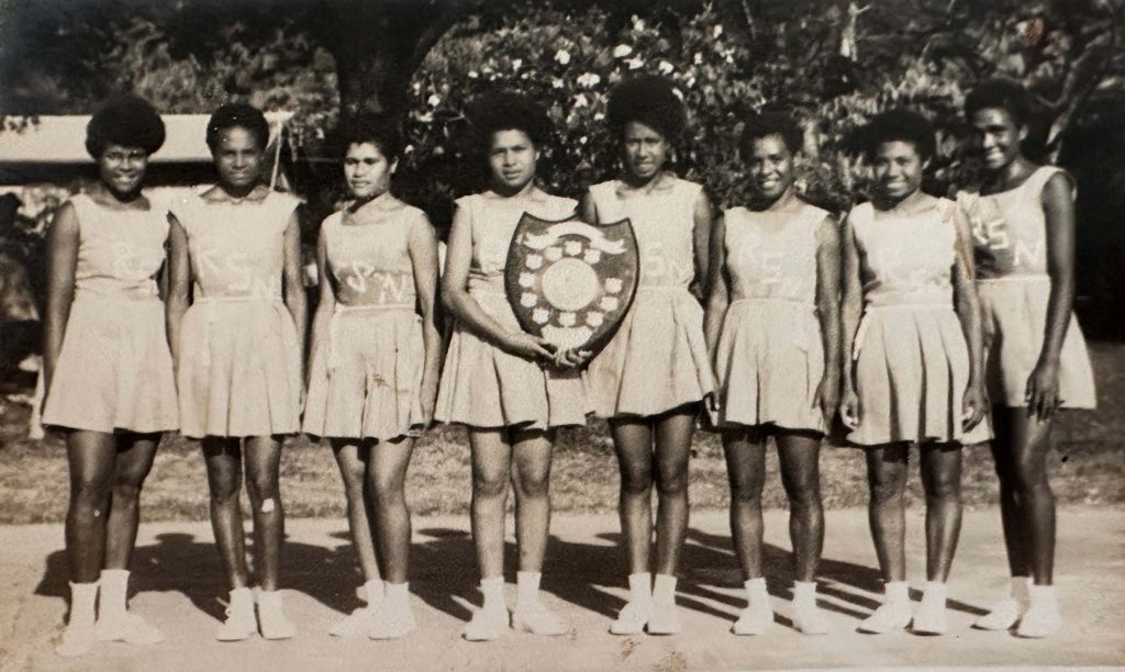 Trainee nurses in PNG in the 1960s wearing basketball attire and holding a competition shield 
