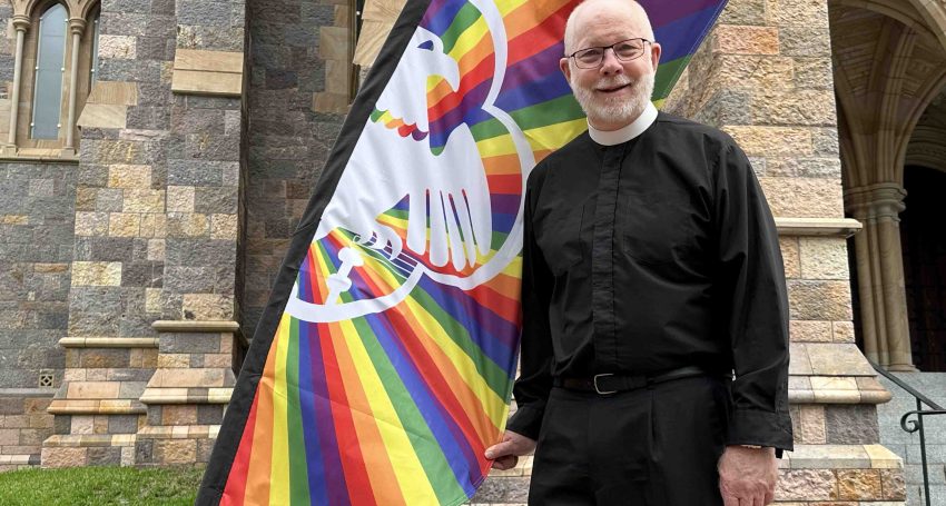 The Very Rev'd Dr Peter Catt with a rainbow flag outside St John's Cathedral in December 2023