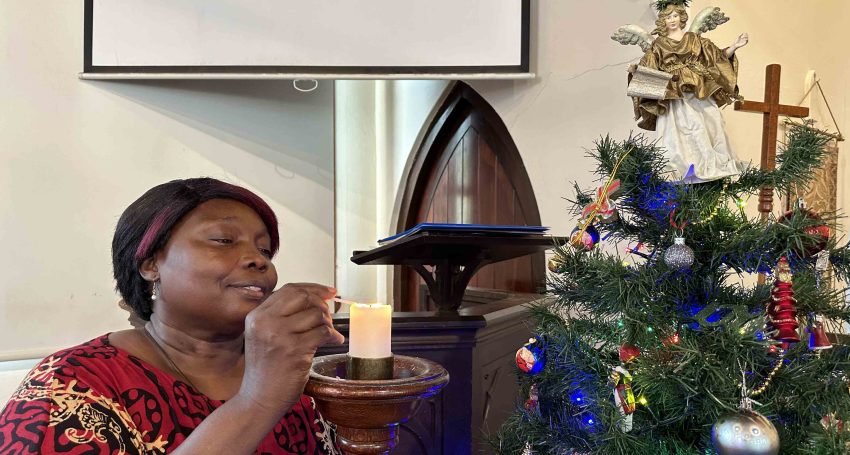 The Rev'd Rebecca King lighting a candle near a Christmas tree