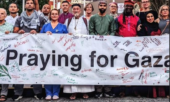 Inter-faith people holding a "Praying for Gaza' sign at a prayer vigil in the city