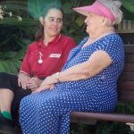 Anglicare nurse in red shirt chatting with elderly woman on park bench
