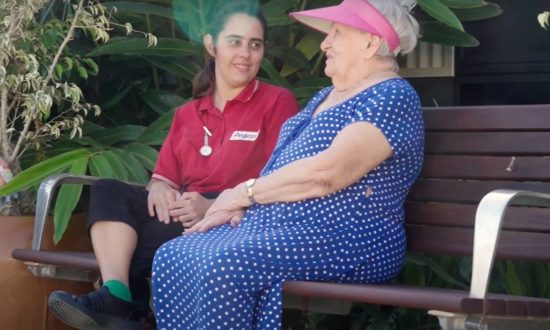 Anglicare nurse in red shirt chatting with elderly woman on park bench