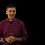 Archbishop Jeremy in p0urple shirt against a black background