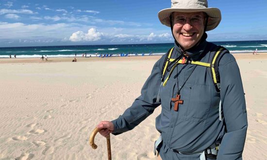 Bishop walking with a walking stick alongside a beach