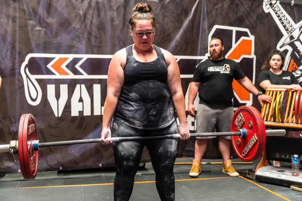 Young woman wearing black lifting a barbell with heavy weights at a powerlifting competition 