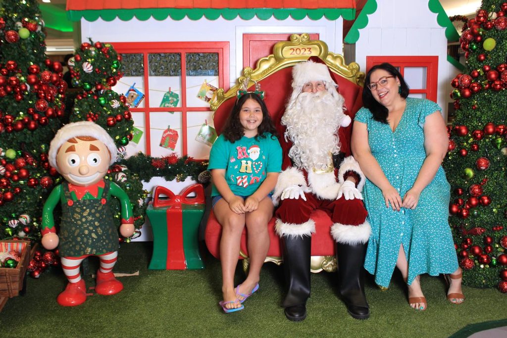 Girl and mother sitting with Santa at a shopping centre 