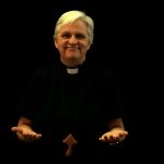 Woman priest with hands open standing against a black background