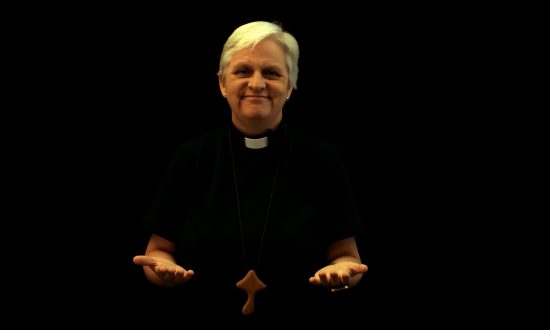 Woman priest with hands open standing against a black background