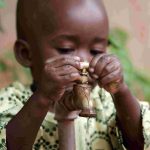 South Sudanese child turning on a tap outside