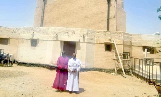 Two Sudanese clergy dressed in robes outside a church in Sudan