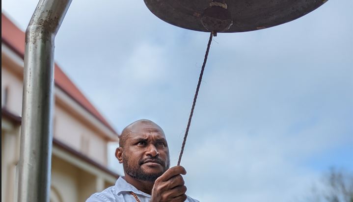 Melanesian man ringing a church bell by pulling on a rope