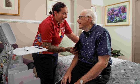 Nurse wearing red shirt taking the blood pressure of an older man in his room