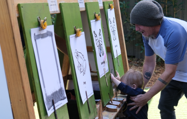 Father wearing a beanie with his young son in front of an art easel