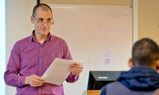 Man wearing purple shirt lecturing in front of a whiteboard