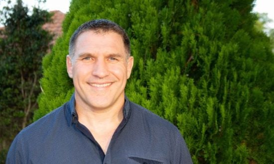 Man in dark blue shirt standing in front of a bush