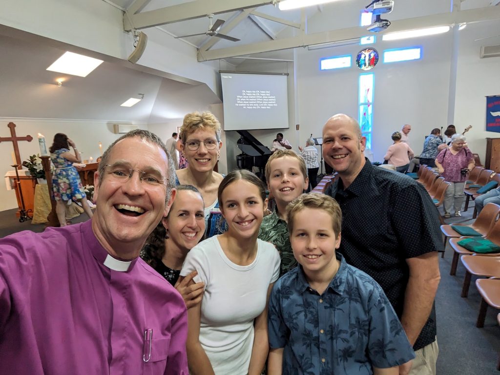 A bishop wearing a purple shirt, teens and their parents in a church on Easter Day