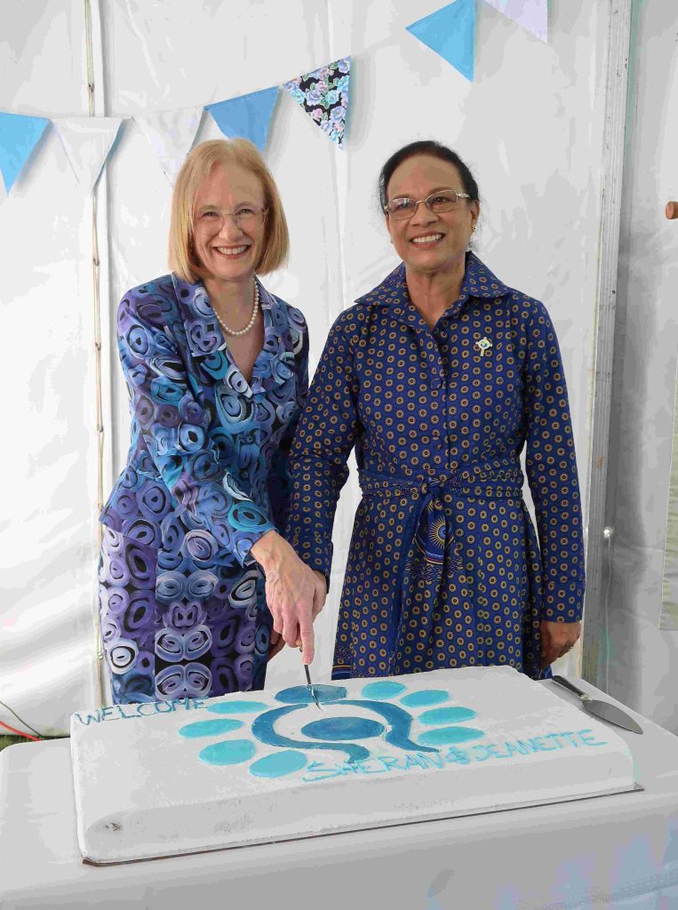 Two women cutting a large white cake at an event