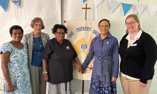 Five women from diverse backgrounds and ages standing in front of a church banner