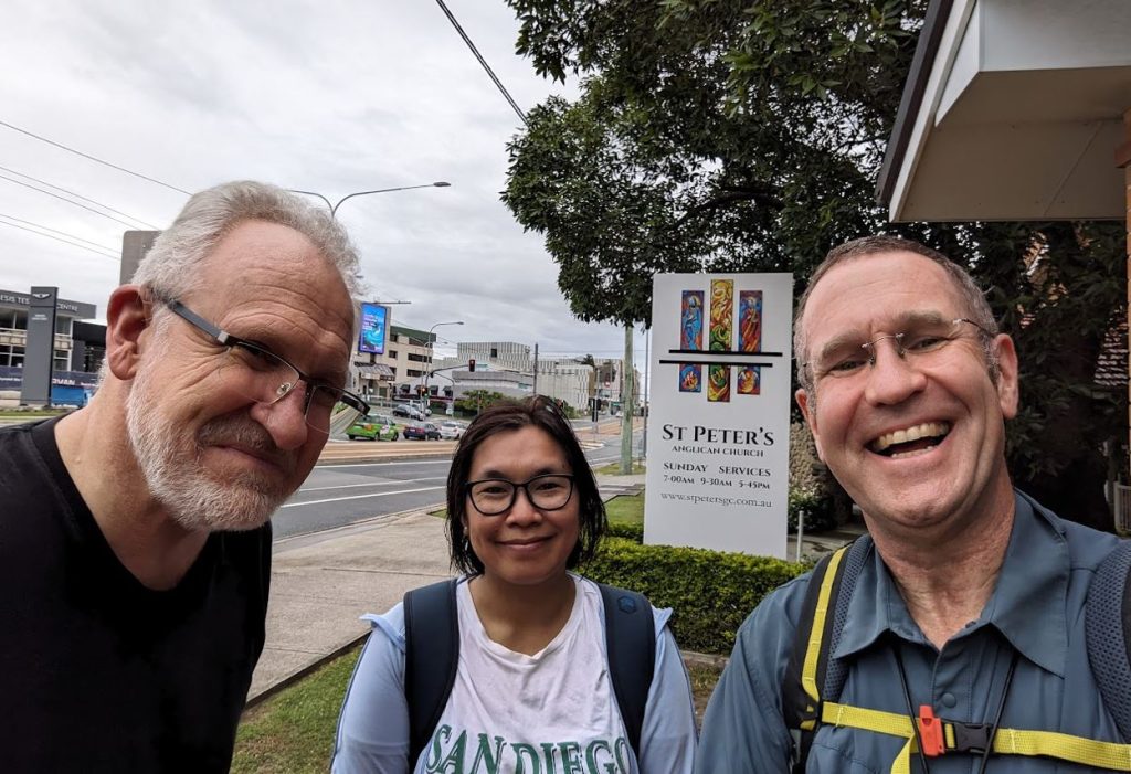 Three people smiling outside a church wearing walking gear