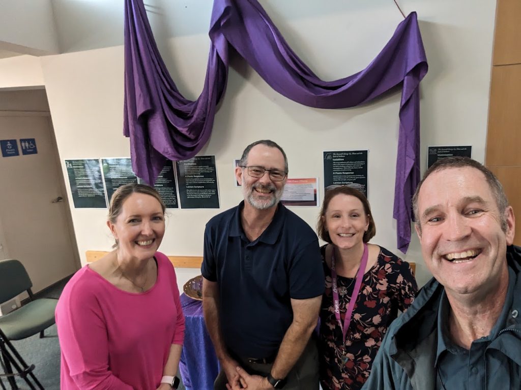 Four people smiling in a church hall with purple fabric hanging on the wall