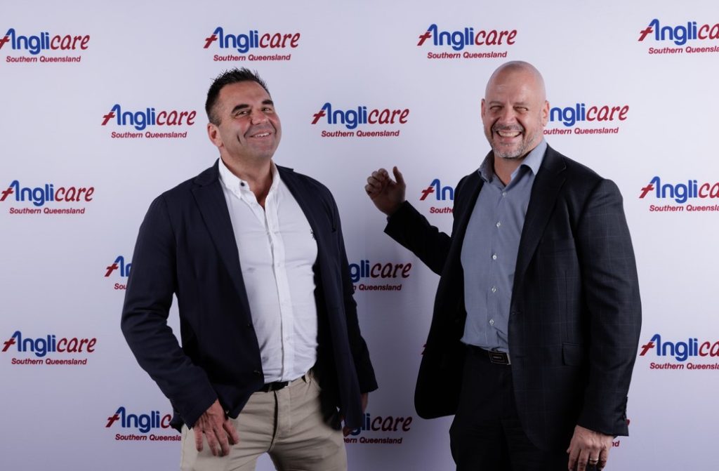 Two men in jackets standing in front of Anglicare signage