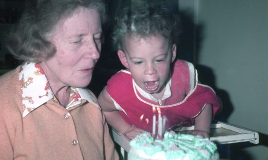 Toddler in the 1970s about to blow out birthday cake candles with grandmother sitting next to him