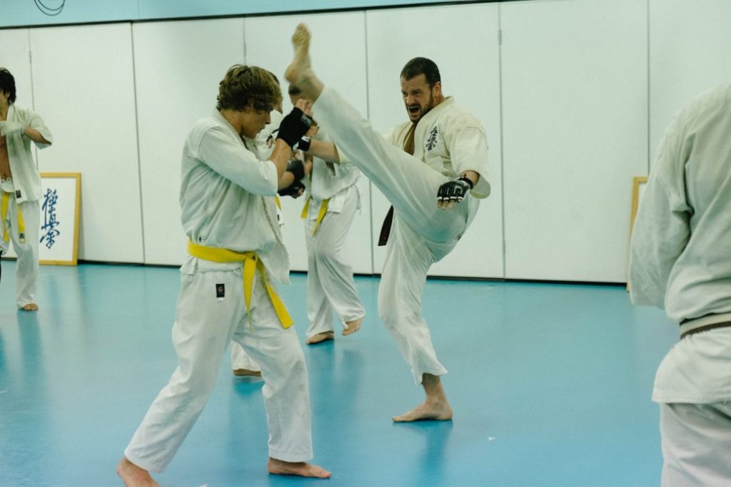 Man doing a karate kick with another man who is wearing gloves 