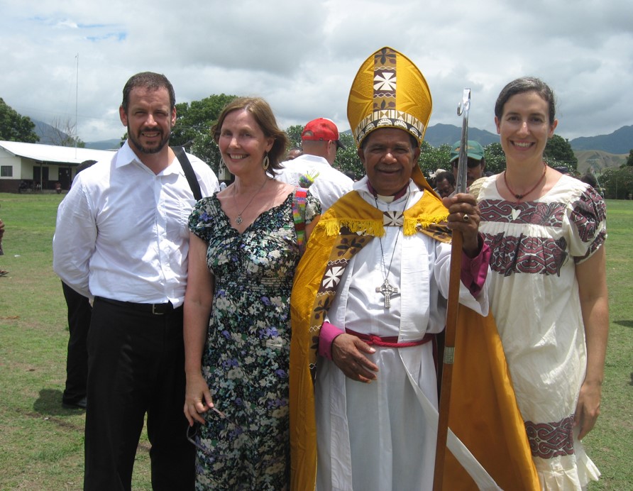 A man and two women gathered with a bishop outside 