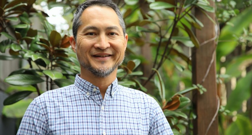 Middle-aged man in plaid blue and white shirt smiling, looking at the camera