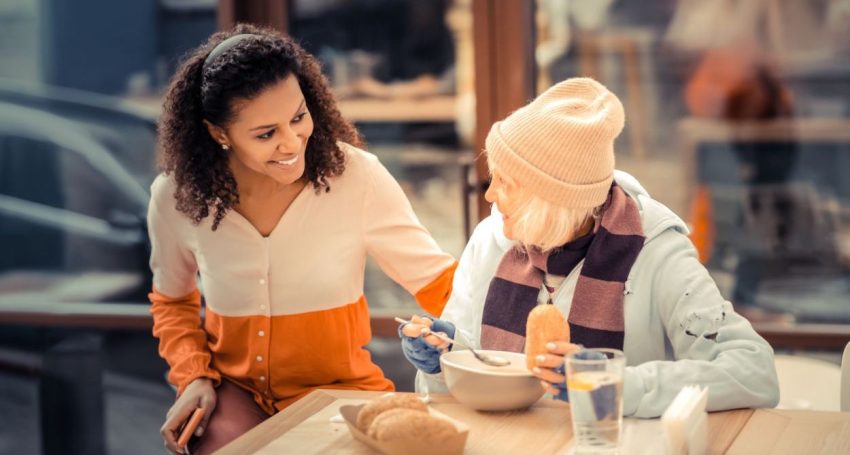 Older homeless woman enjoys conversation with young woman while having a meal