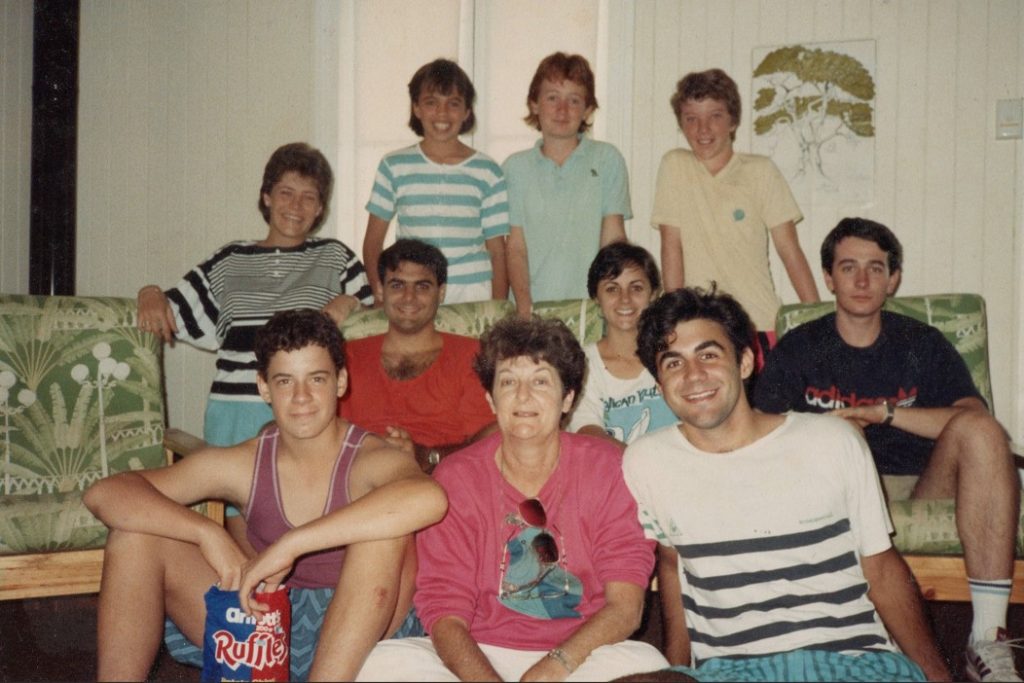 Large group of young people with a mother sitting and standing in a lounge room in the 1980s