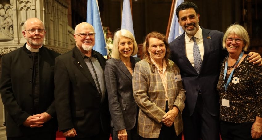 Six people in front of a cathedral sanctuary smiling while looking at the camera