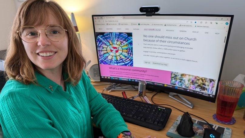 Woman priest in green blouse in front of a PC smiling