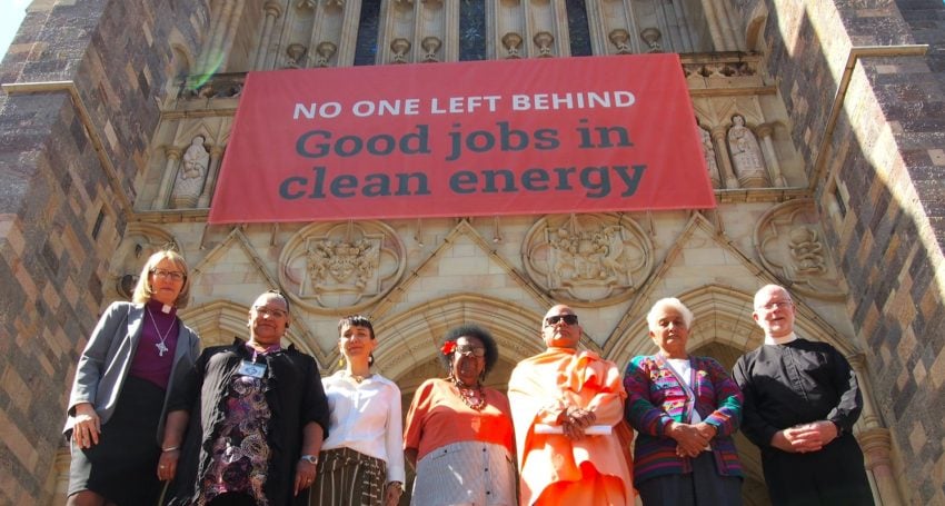 Seven inter-faith leaders outside a Cathedral standing under a banner calling for clean energy