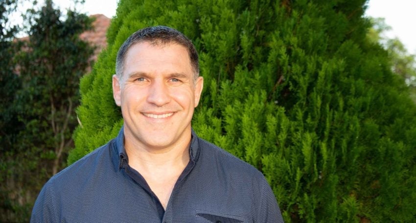 Man in dark blue shirt standing in front of a bush