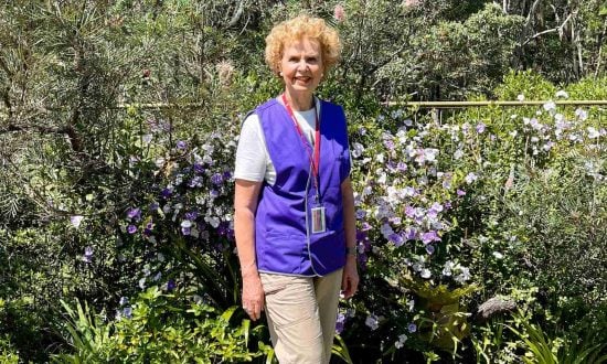 Woman wearing a lanyard and purple high-vis vest next to bush