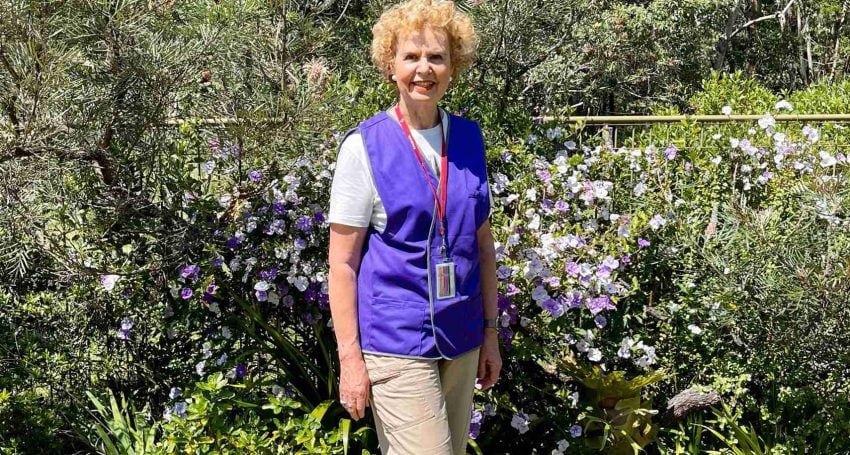 Woman wearing a lanyard and purple high-vis vest next to bush