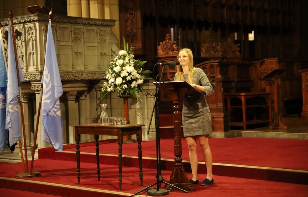 Woman in light grey dress speaking into a microphone in a cathedral