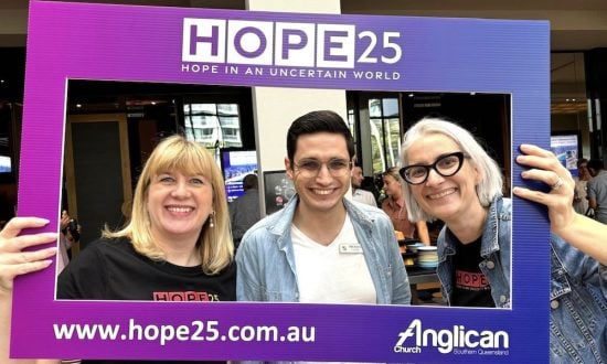 Two women preists and a man priest behind a photo board smiling