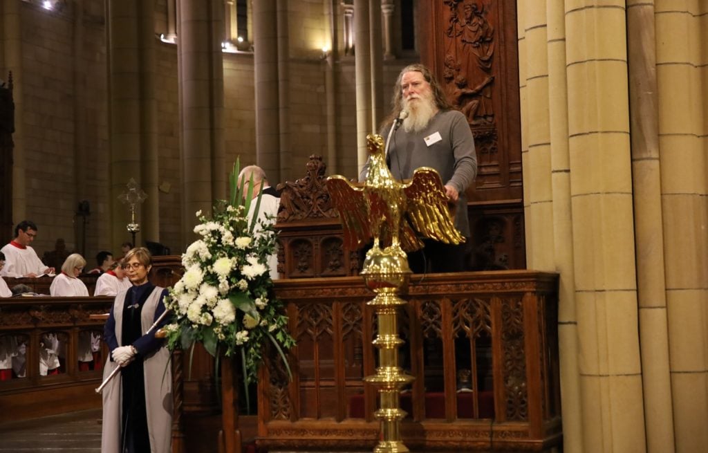 Man in grey jumper leading prayers in a Cathedral service 