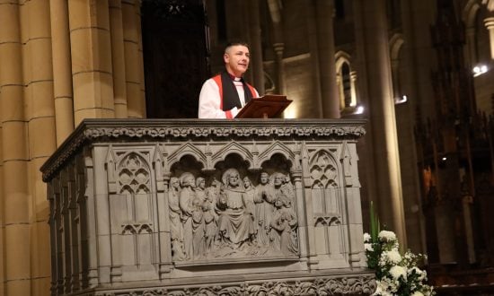 Archbishop wearing robes while giving a sermon in an ornate cathedral pulpit