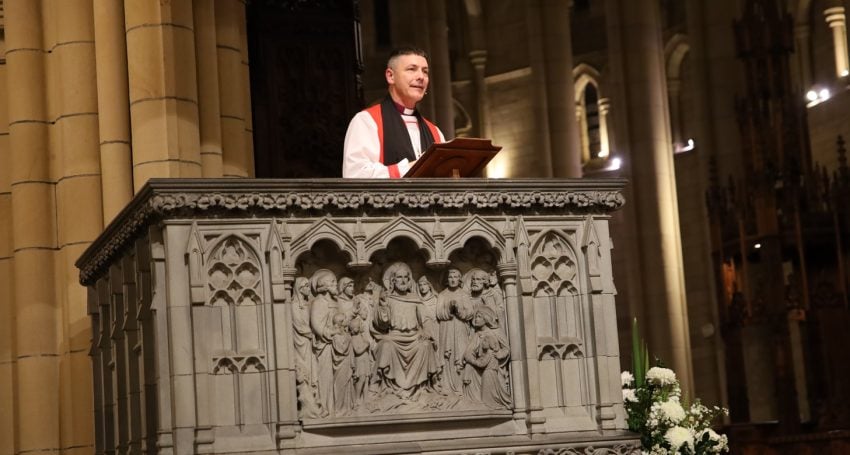 Archbishop wearing robes while giving a sermon in an ornate cathedral pulpit