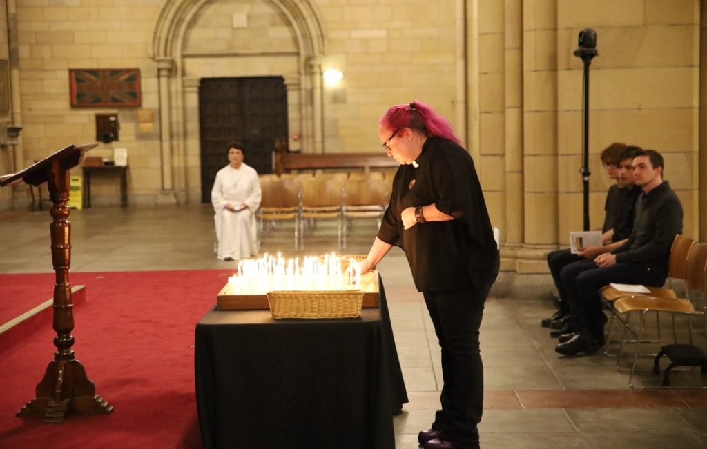 Woman priest in black clothes lighting a candle in a cathedral service 