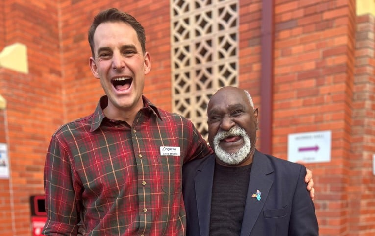 Two men laughing and hugging near a red brick wall