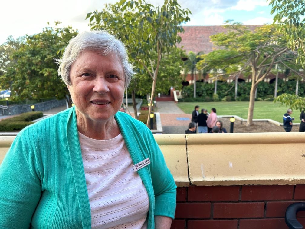 Woman in green cardigan and white t-shirt near a school courtyard 