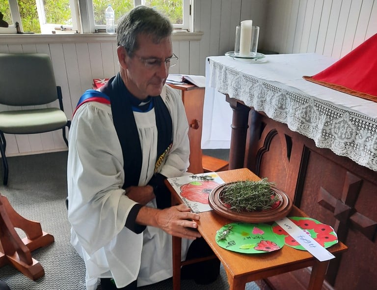 Priest in robes with a bowl of rosemary in front of a church altar on Remembrance Day 