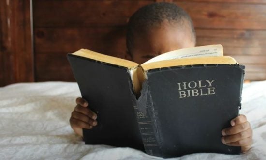 Young boy reading an old Bible in bed