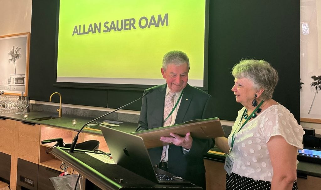 Husband and wife in front of a lectern, with the man holding an award