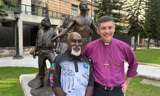 Anglican bishop and Torres Strait Islander elder in front of a wartime memorial